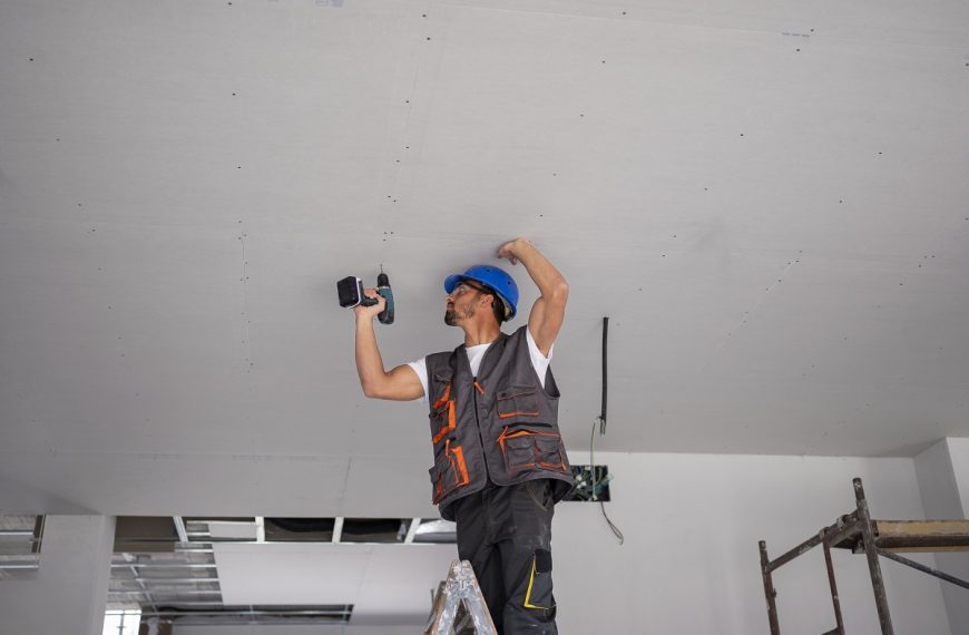 man wearing a blue hard hat drilling into a ceiling